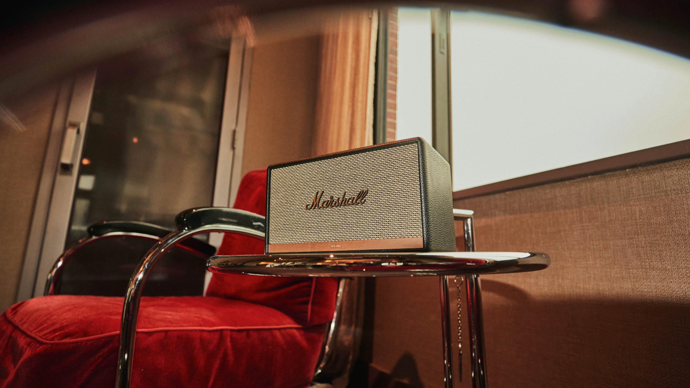 Ein Marshall-Verstärker steht auf einem Glastisch mit einem Schlagzeug im Hintergrund, auf dem die Knöpfe und das Lautsprechergitter zu sehen sind.