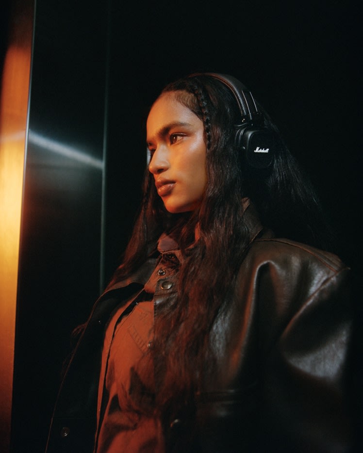 Una mujer con auriculares Marshall Major V Brown y chaqueta oscura en un ascensor.
