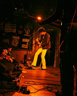 Un hombre toca con su banda en un pequeño local bajo un foco naranja