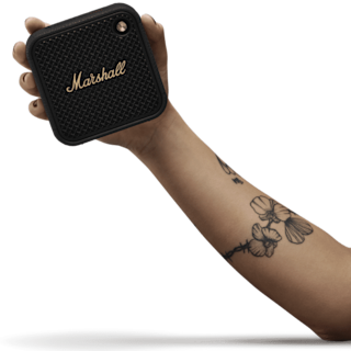 A hand holds Marshall Willen II Black and Brass portable bluetooth speaker.