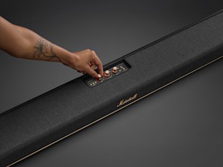 A man reading a magazine in a living room with a TV and Marshall Heston 120.