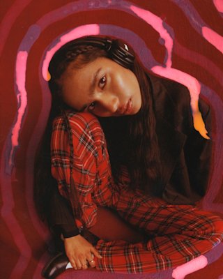 Frau in einem karierten Outfit, sitzend und mit Marshall Major V Black On-Ear-Kopfhörern.