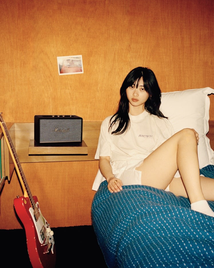 A girl sitting on a bed next to a Marshall ACTON III BLACK guitar.