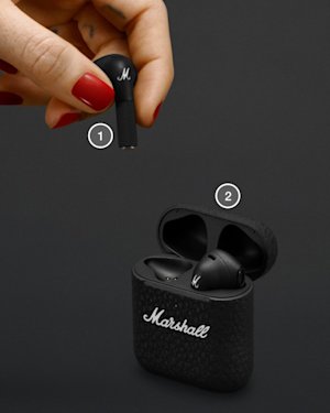 Hand with red painted nails placing a Minor III earbud in their charging case.