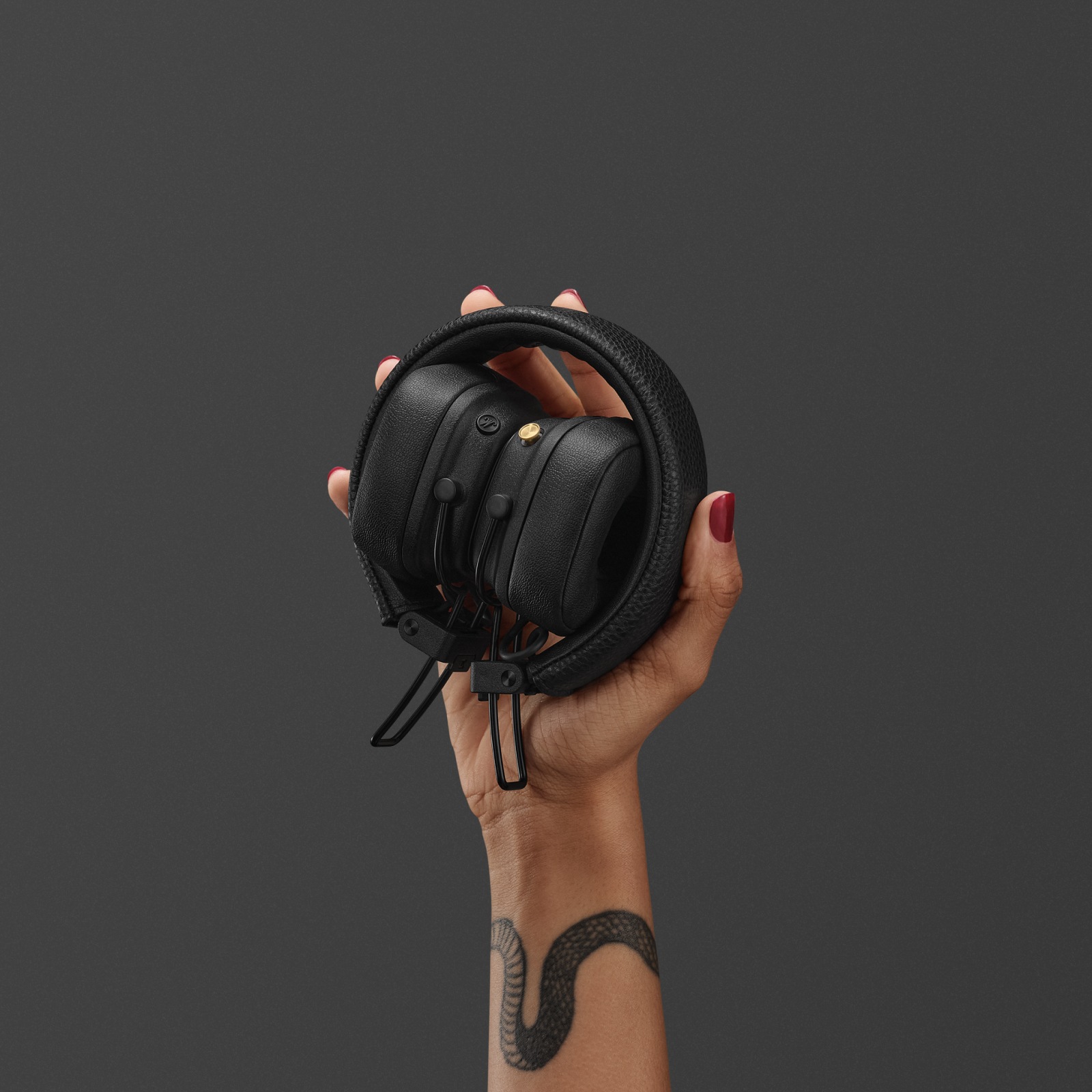 Woman holding a pair of folded black Marshall Major V on-ear headphones against a grey background.