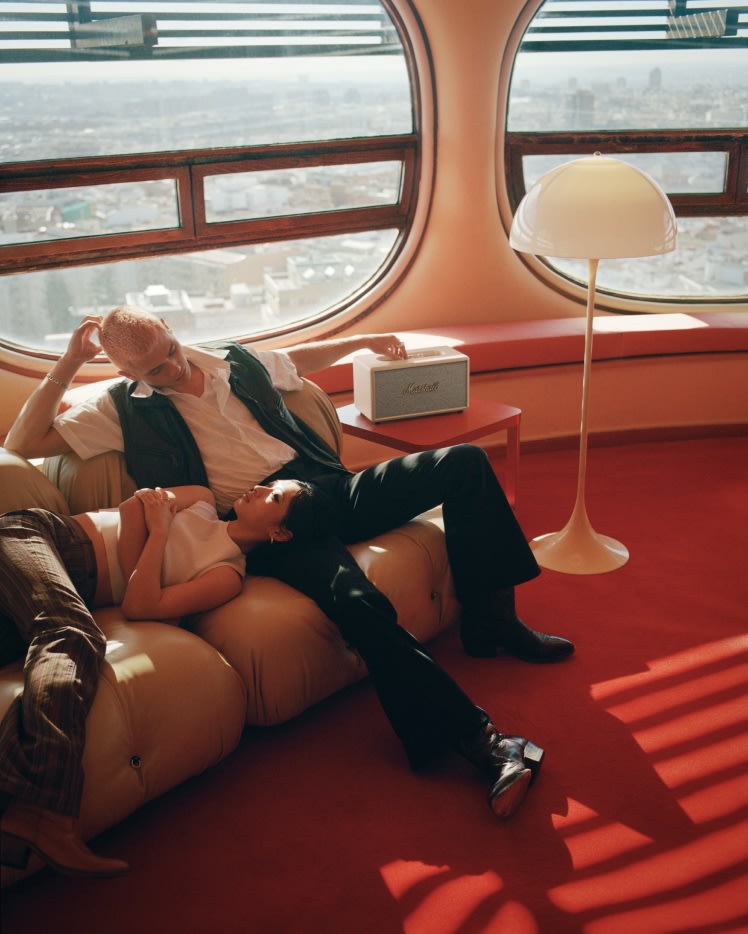 Ein Mann und eine Frau machen es sich auf einer Couch bequem, während sie Musik aus einem weißen Marshall Stanmore III Cream Home Speaker hören.