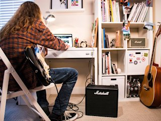 A long haired person in a chessed shirt playing guitar using the Marshall CODE25 Combo