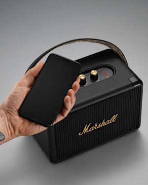 Una mano con tatuajes sostiene un teléfono móvil delante de un altavoz de Kilburn II.