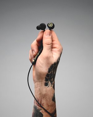 Una mano tatuada sosteniendo un par de auriculares Marshall Mode EQ con cable.
