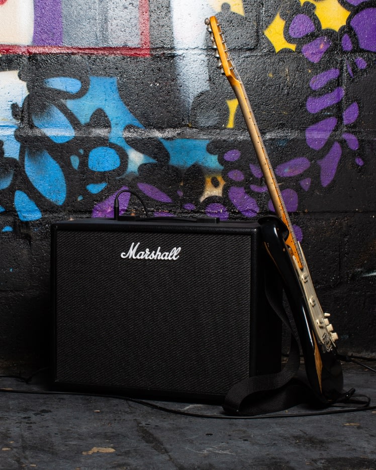 Front view of the Marshall CODE50 Combo and guitar in front of graffiti wall.