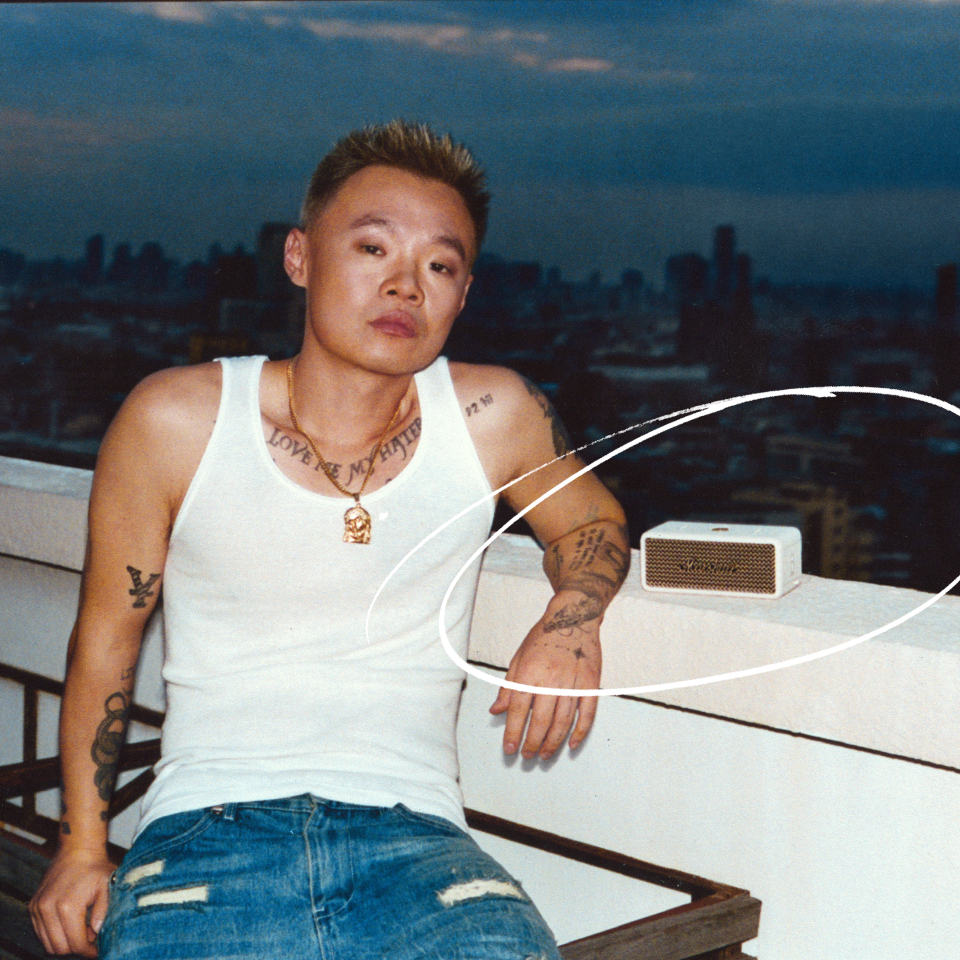 Bohan Phoenix est assis sur un balcon, avec un paysage urbain en arrière-plan et un haut-parleur portable Marshall.