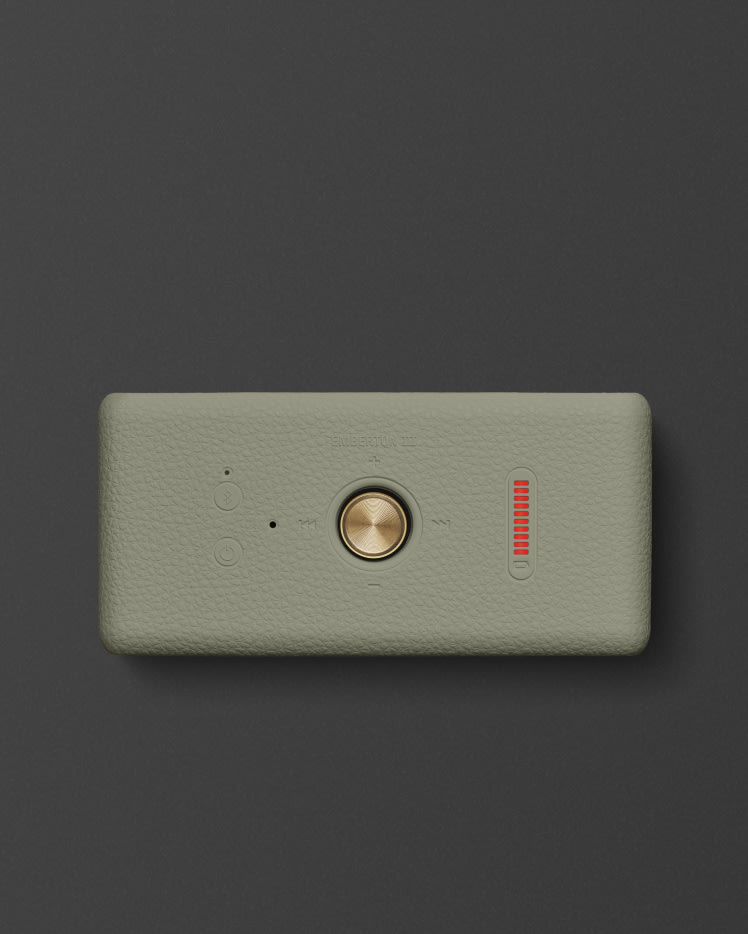 Top view of Marshall Emberton III Sage, featuring a gold knob in the center, a red vertical volume indicator, and two circular buttons set against a dark grey background.