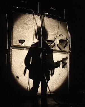 A young Jimi Hendrix playing guitar on stage with a Marshall stack behindd