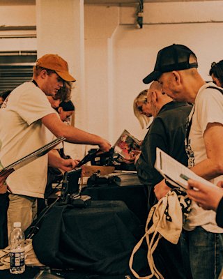 People gather around a table examining and exchanging vinyl records and papers at an indoor event.