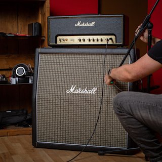 Person adjusting a microphone in front of a Marshall guitar amplifier stack.