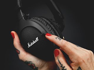 A woman holding a pair of black MONITOR II ANC headphones in a Marshall frame.