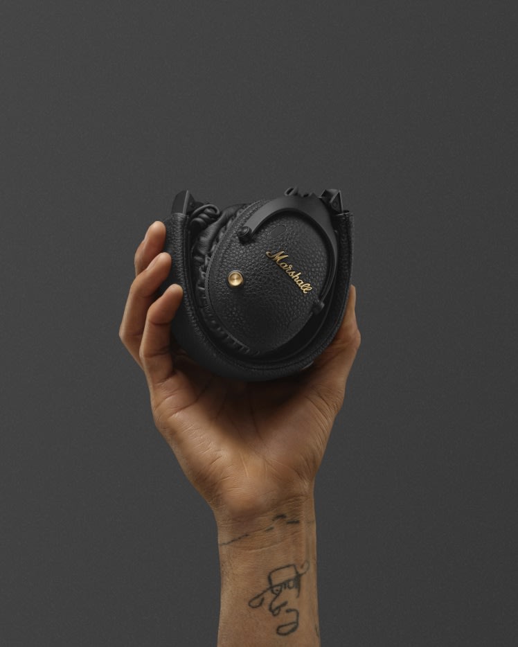 Un par de auriculares over-ear bluetooth Marshall Monitor III A.N.C. Black doblados en una mano sobre un fondo gris oscuro.