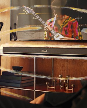 TV with a Heston 120 soundbar below it on a wooden shelf, while books and decor fill the lower shelves.