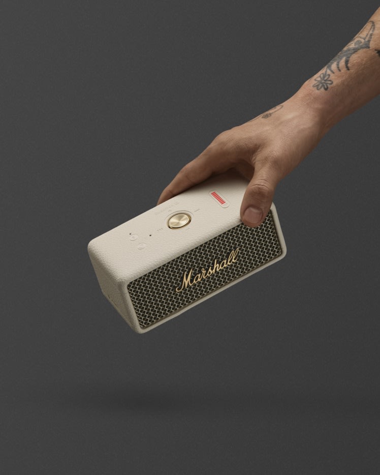A hand holding Marshall Emberton III Cream speaker against a dark background.