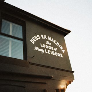 Una proyección de luz nocturna proyecta el texto "deus ex machina - la logia del ocio pesado" sobre el lateral de la fachada de un edificio.