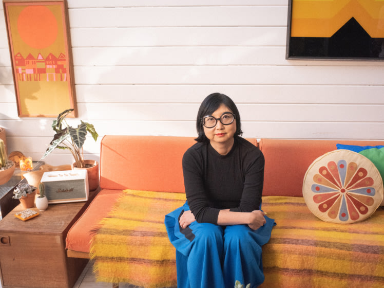 Shirley Kurata sits in a orange couch.
