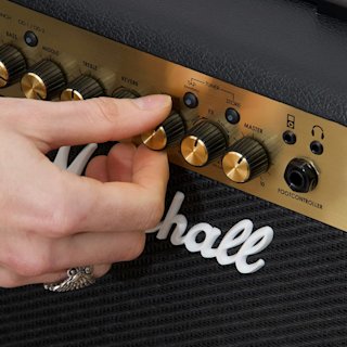 Una mano girando el mando de volumen de un amplificador Marshall MG