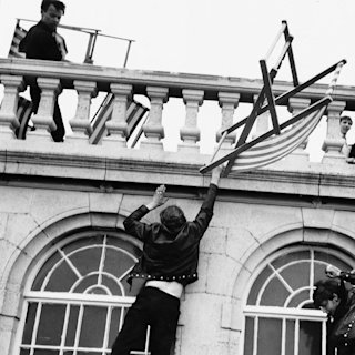 Image en noir et blanc d'une personne grimpant sur le mur d'un bâtiment.