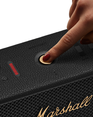 A gold power button on Marshall Middleton II Black and Brass Bluetooth speaker with a textured surface.