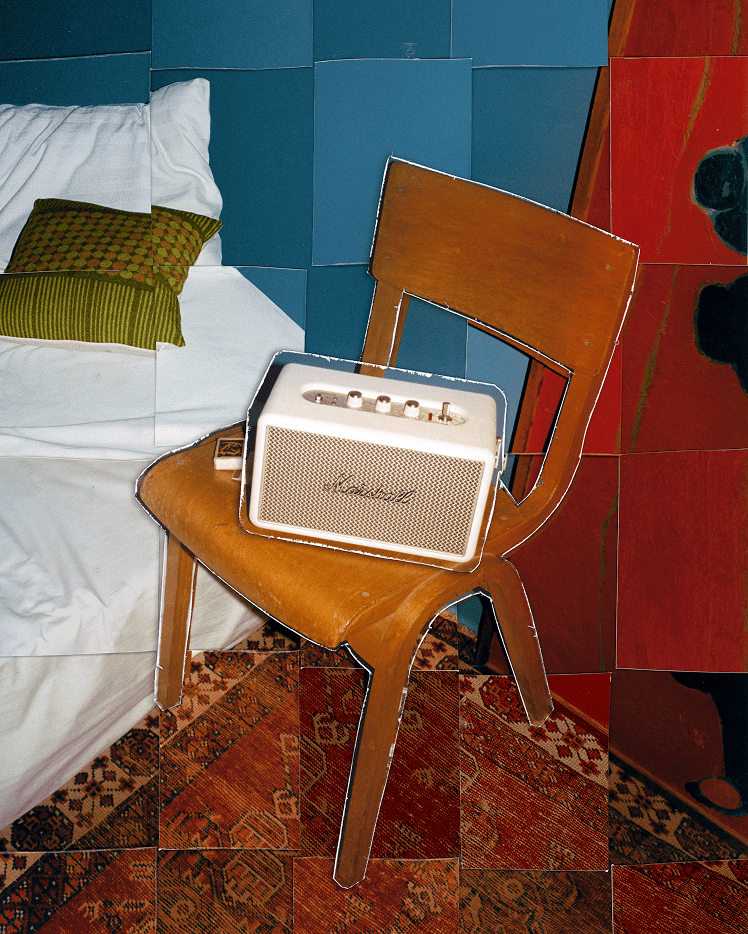 Marshall Kilburn III Cream portable speaker rests on a wooden chair by a bed with white bedding and a green pillow.