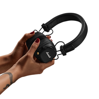 Frau hält ein Paar schwarze Marshall Major V On-Ear-Kopfhörer vor einem dunklen Hintergrund.