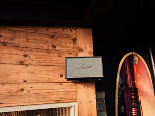 Un altavoz Marshall montado en una pared de madera junto a un letrero de una tabla de surf, con iluminación ambiental.