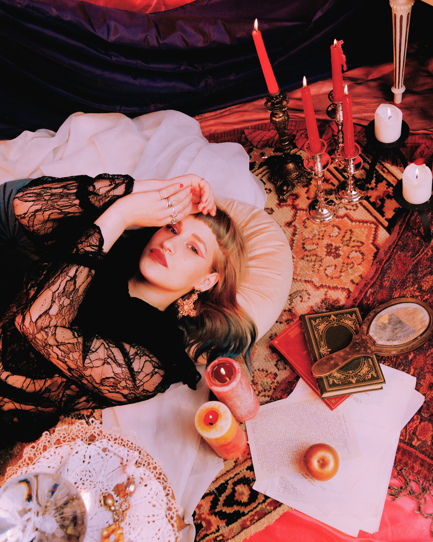 촛불에 둘러싸인 카펫 위에 누워 있는 아티스트 아이코