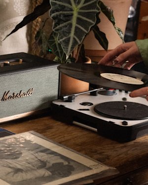 A person changing a vinyl on their record player connected to a Marshall speaker.