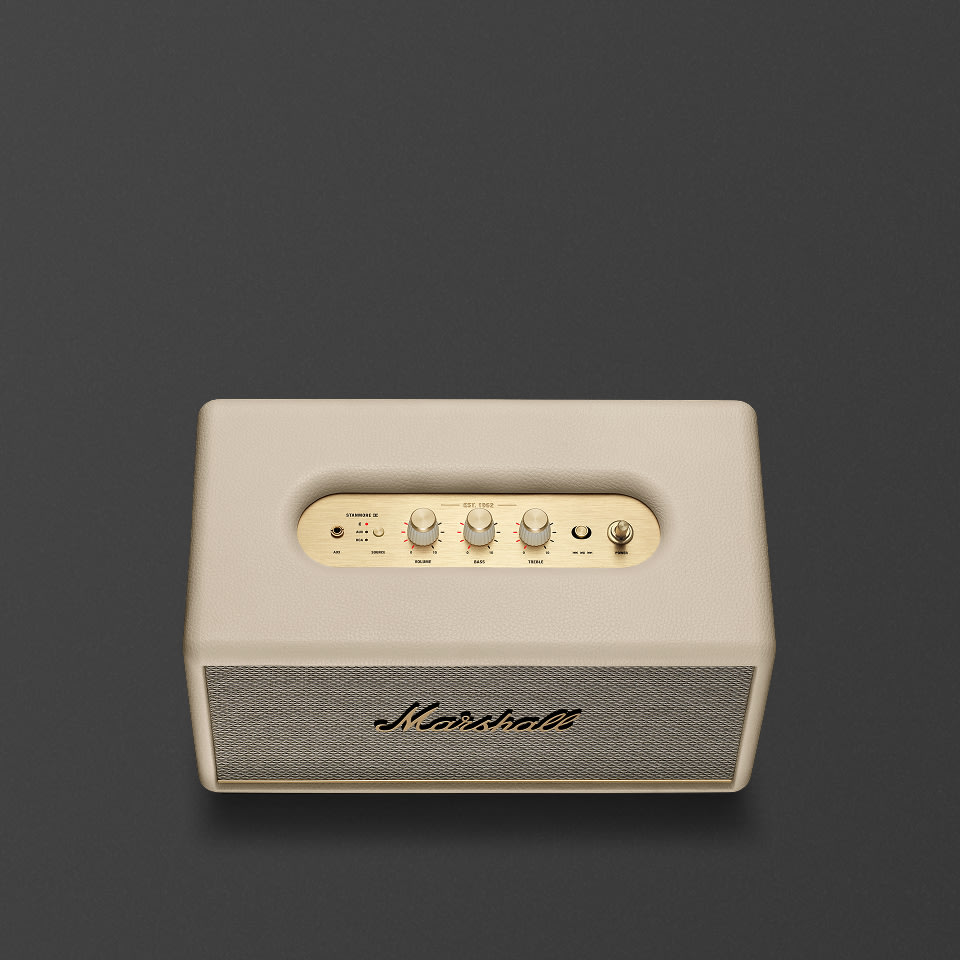 A Marshall Stanmore III Bluetooth home speaker in cream with brass accents and control knobs is shown against a plain dark gray background.