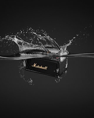 Marshall Emberton III Black and Brass bluetooth speaker partially submerged in water, with splashes around it.