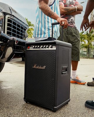 People stand by a parked car with the Marshall Bromley 750 party speaker between them.