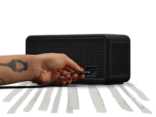 Pluging a cable into the back of the Marshall Middleton II Black and Brass portable Bluetooth speaker on a black and white striped surface.