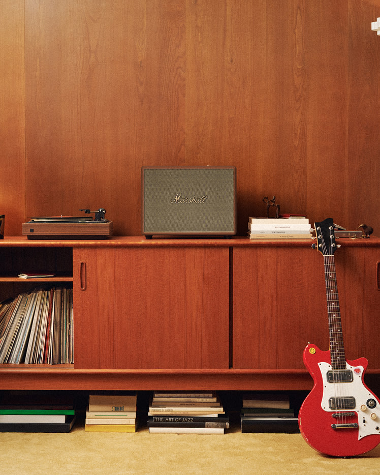 A red electric guitar leans against a wooden cabinet featuring a Marshall Woburn III Brown speaker.