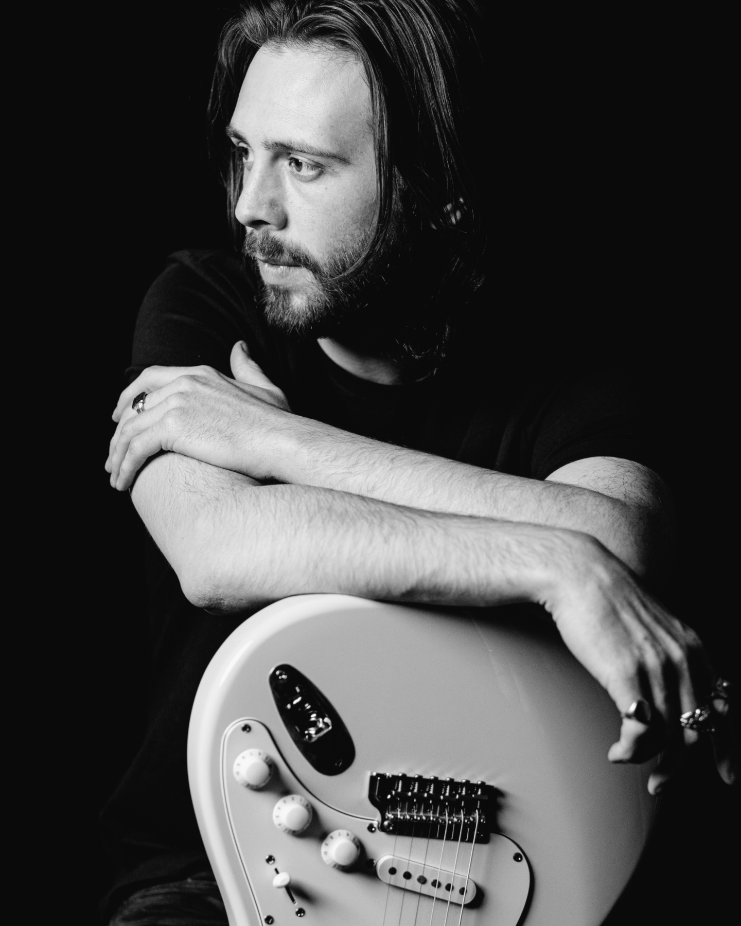 Artist Laurence Jones holds a guitar and looks to the side. He is wearing a black shirt and rings on his fingers.