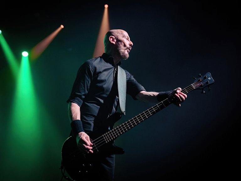 A musician plays an electric bass guitar on stage under colourful spotlights.