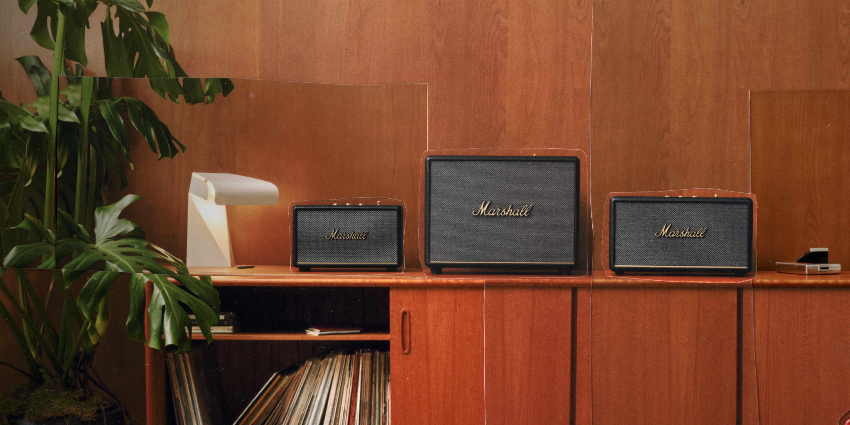 Three Marshall home speakers are placed on a wooden cabinet with shelves below holding vinyl records and books.