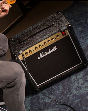 Person seated with a guitar, connected to a Marshall DSL5 amplifier placed on the floor.