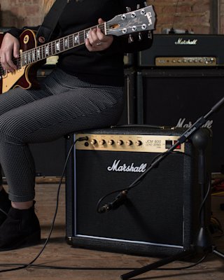 A woman is sitting next to a Marshall Studio Classic Combo amplifier.