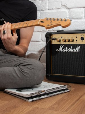 A man playing an electric guitar next to a Marshall MG10 amplifier.