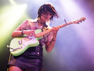 Yvette standing in front of a smoky background playing guitar