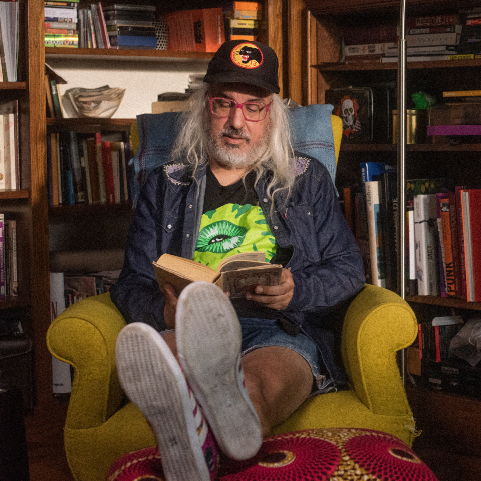 J Mascis sitting in a chair reading a book.