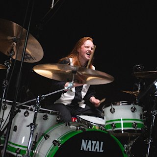 Sam Ogden playing on a white and green Natal drums kit white and green