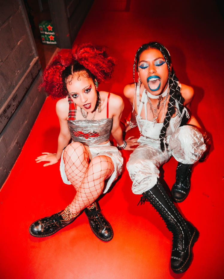 The 'Nova Twins' band sitting on a red carpet floor