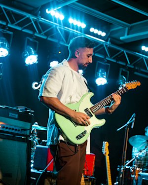 Un guitarrista con camisa blanca tocando su guitarra verde en un pequeño local