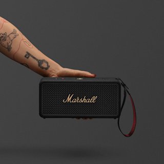 An image of a tattooed arm holding a Marshall Middleton II portable speaker in Black and Brass.